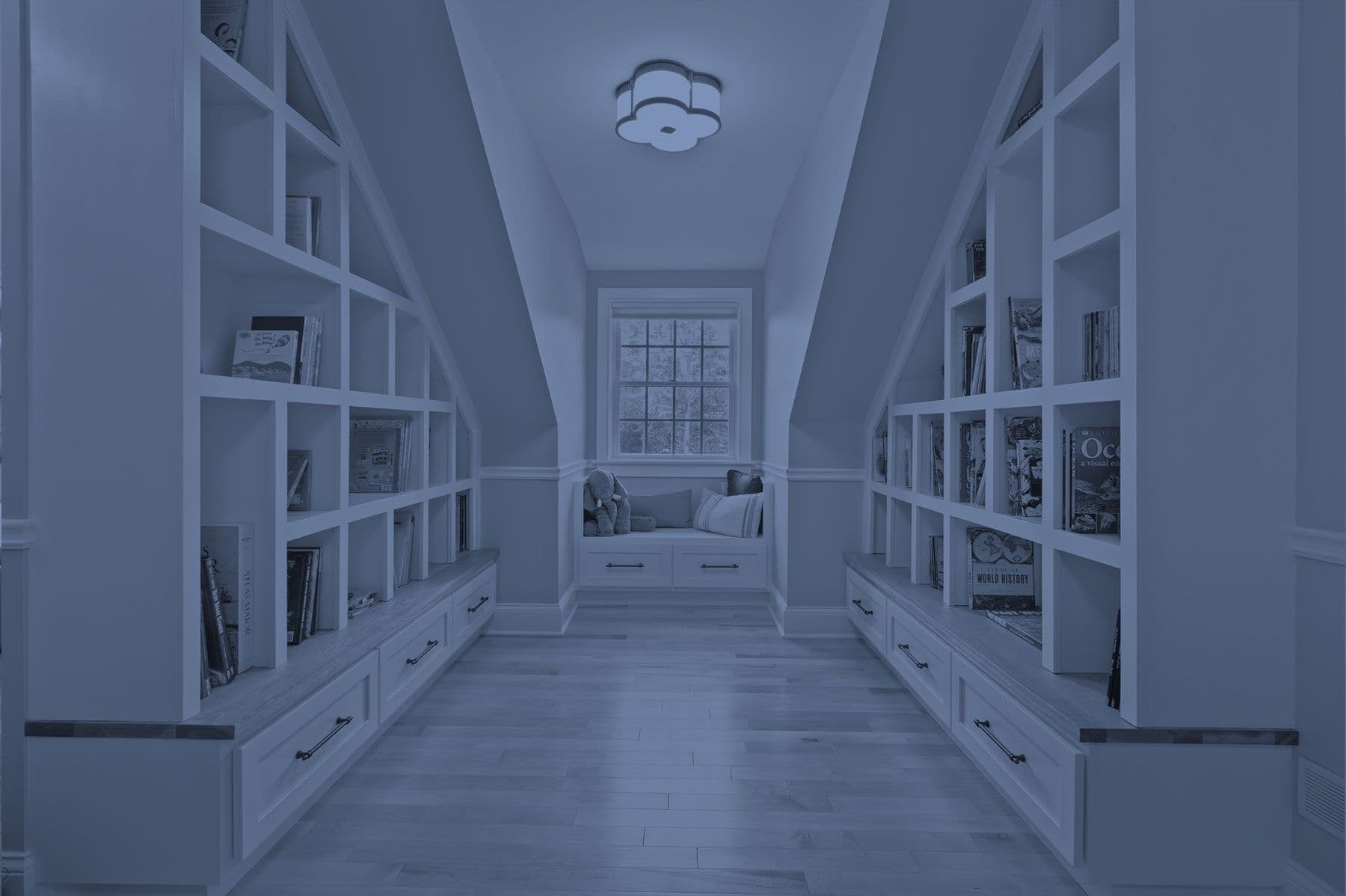 Custom millwork installation featuring symmetrical reading nook layout with floor to ceiling book shelves and drawers, mix of painted white cubbies and drawers with natural wood tops.