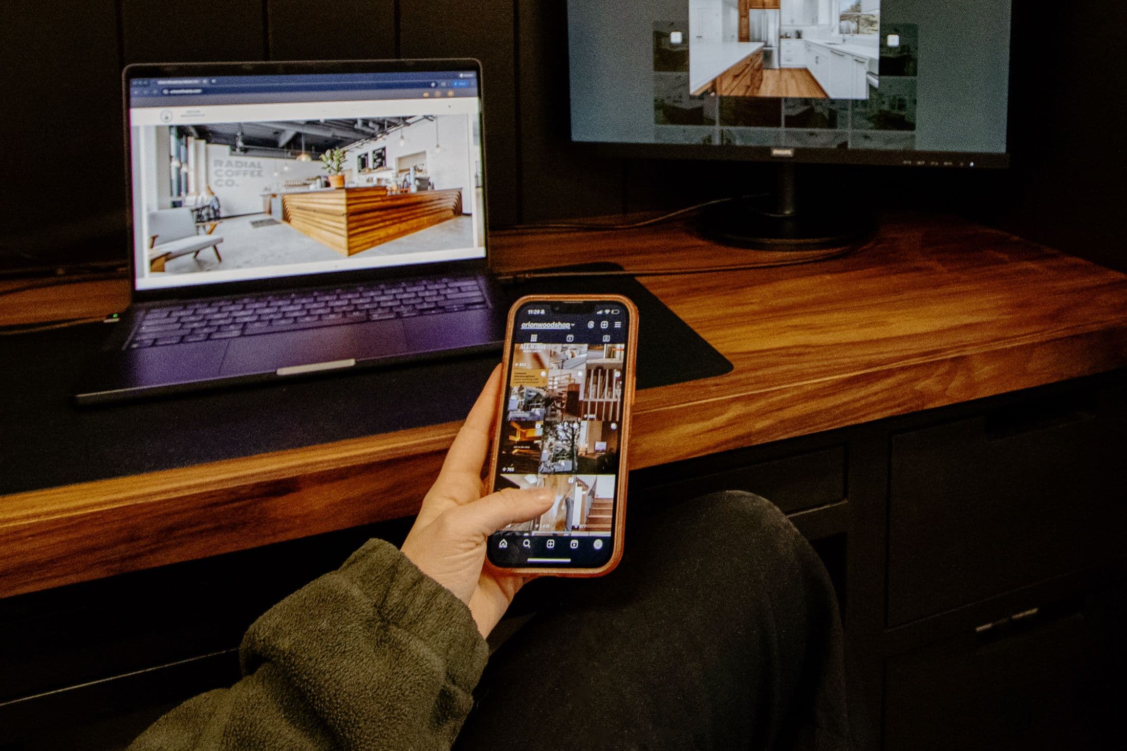 Scrolling Orion Woodshop Instagram page on an iPhone, with Orion Woodshop Website Homepage and Portfolio page on the computer in the background.